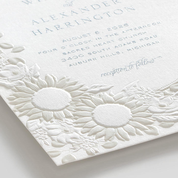 A wedding invitation with embossed sunflowers and a sunburst frame around the wording