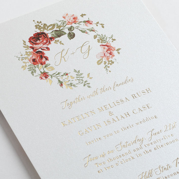 A sophisticated wedding invitation with a vibrant red and green floral crest framing an elegant monogram