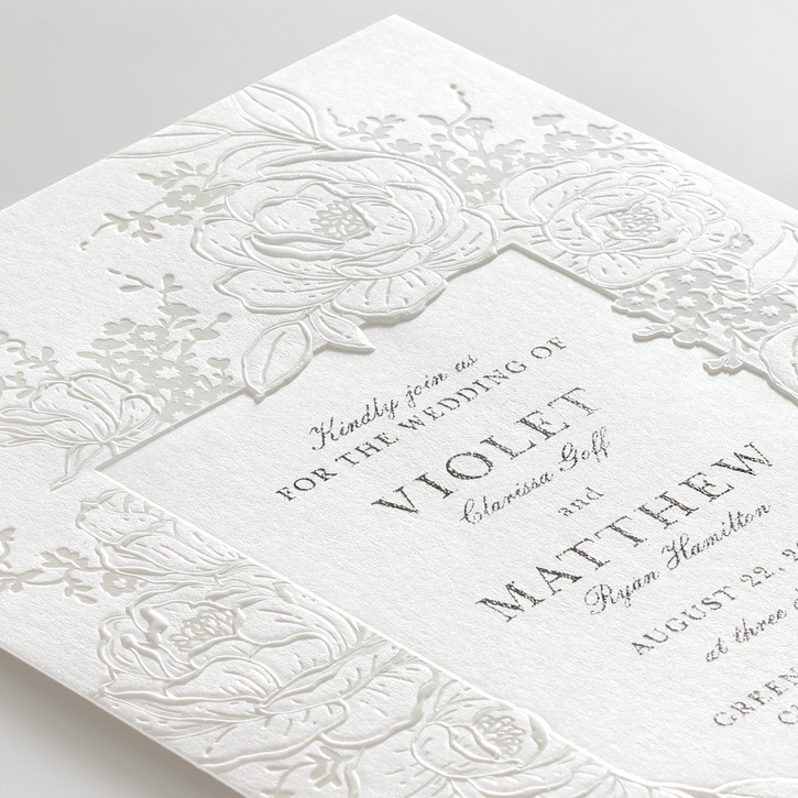 Wedding invitation featuring a debossed panel framed by a delicate floral design embossed with pearl foil