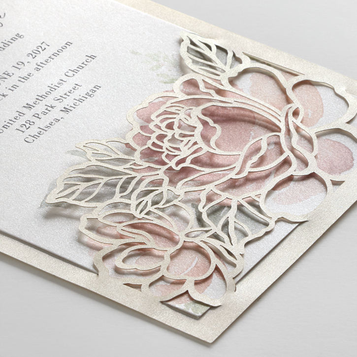 – A delicate laser cut backer adds depth to a wedding invitation featuring pastel peonies