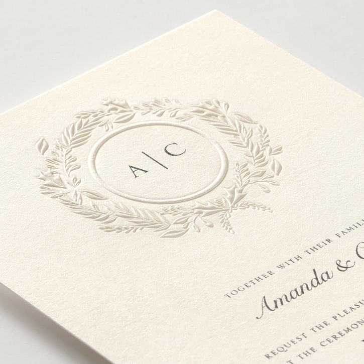 Elegant wedding invitation featuring a delicate foil-embossed wreath and a monogram printed in raised thermography ink.