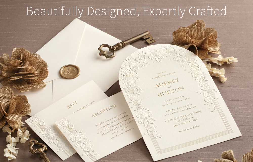 An arch-shaped wedding invitation with intricate floral embossing shown with matching enclosures and envelope with wax seal.