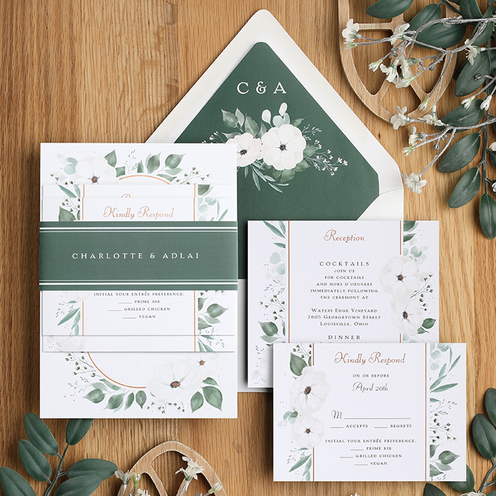 A belly band invitation suite with trendy greenery design is shown with coordinating pieces.