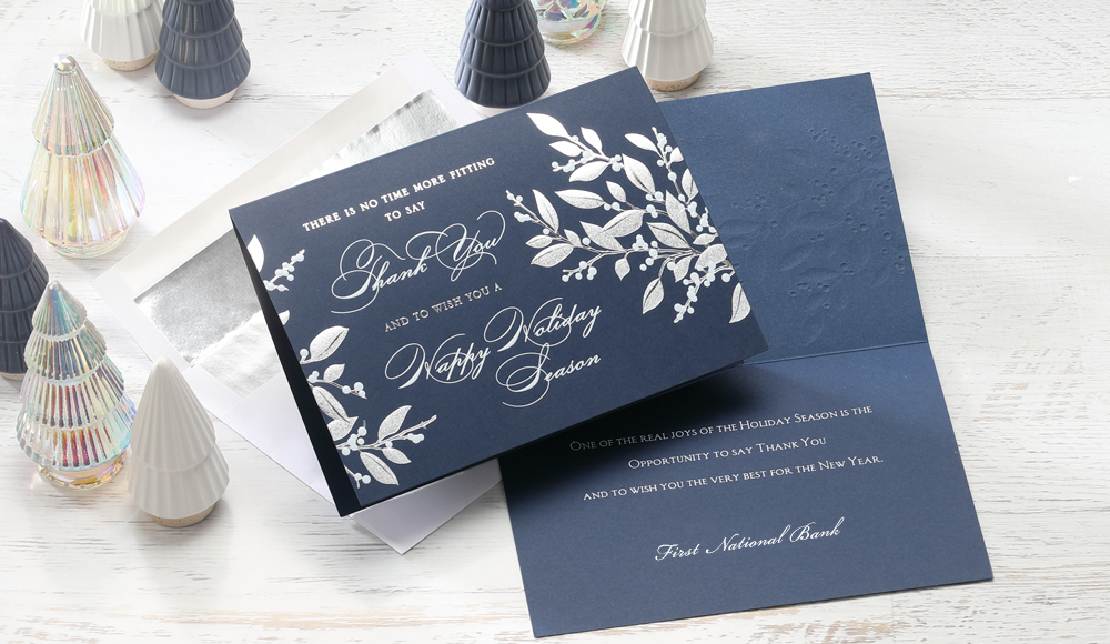 A personalized business holiday card in dark blue with white printed greenery and personalization.