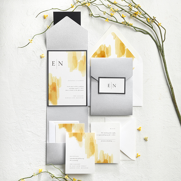 A silver shimmer pocket with wedding invitation featuring yellow brushstrokes is striking.
