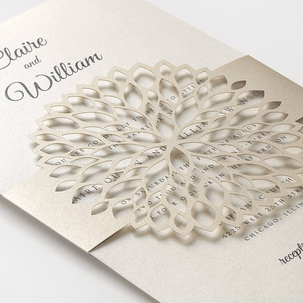 A gold, laser cut flower belly band wraps around a gold invitation for a non-traditional wedding invitation.
