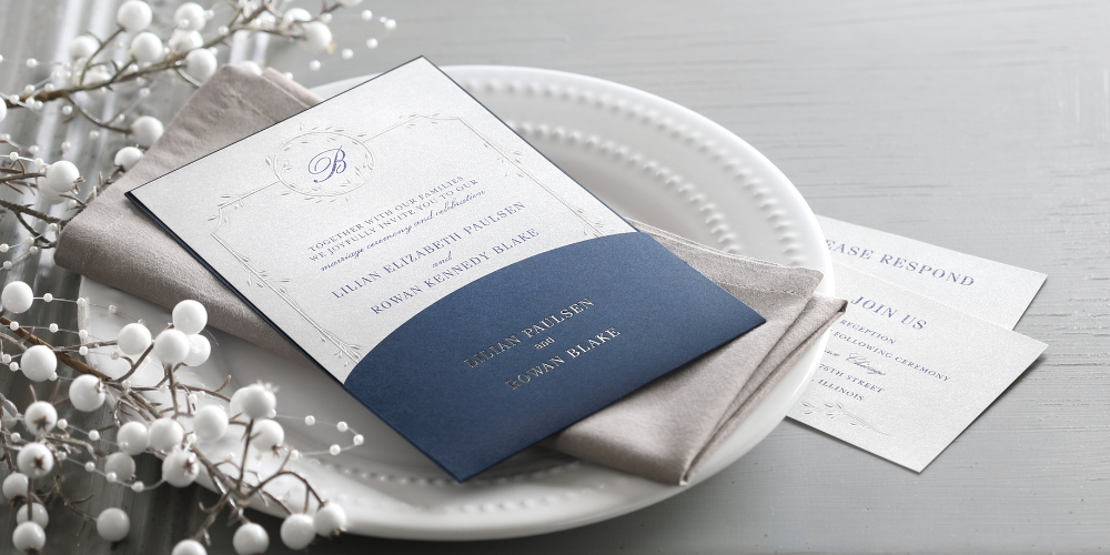 An embossed wedding invitation in a navy blue pocket with foil printing.